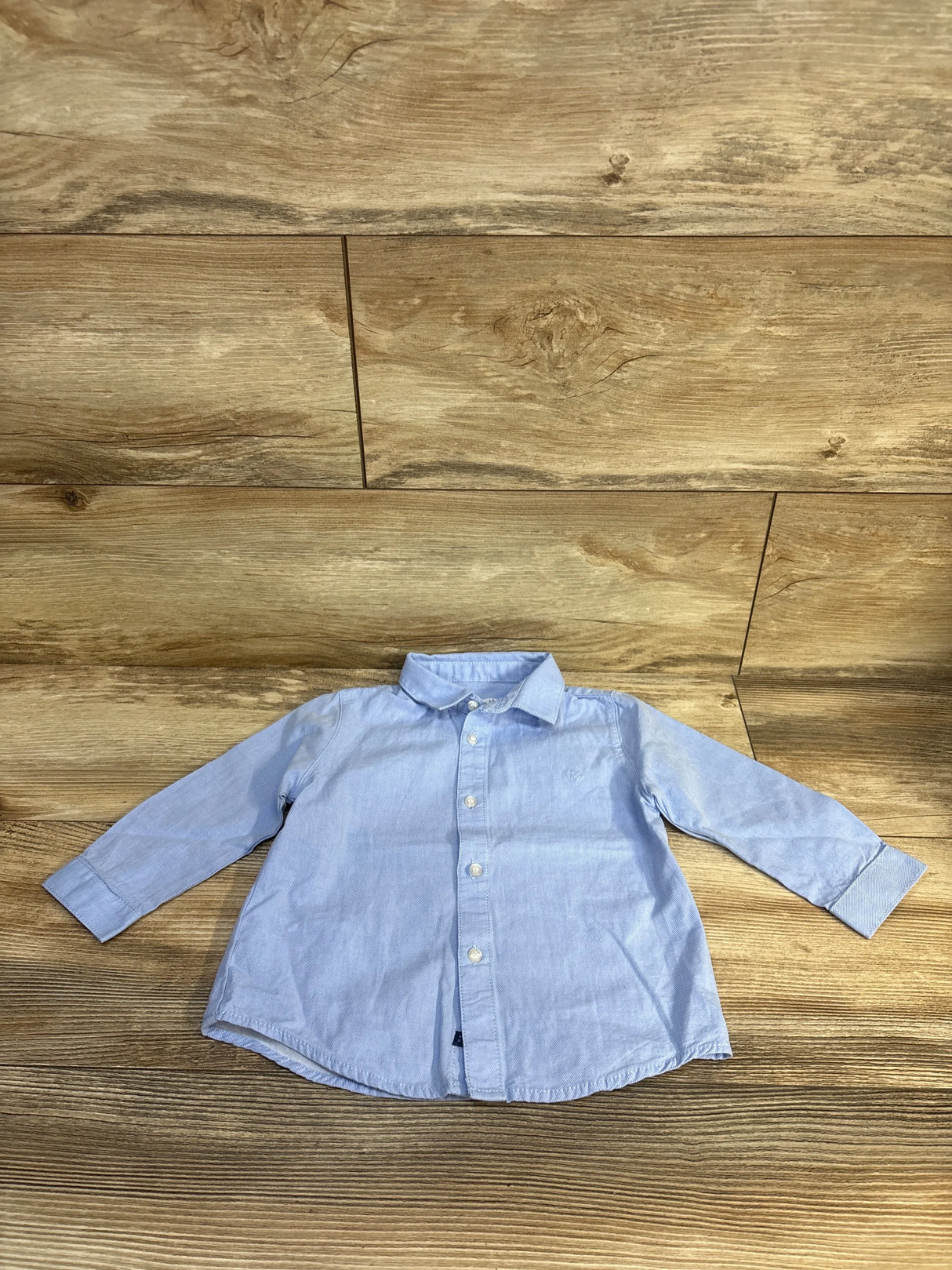 Light blue boys button-down shirt with long sleeves, laid flat on wood floor