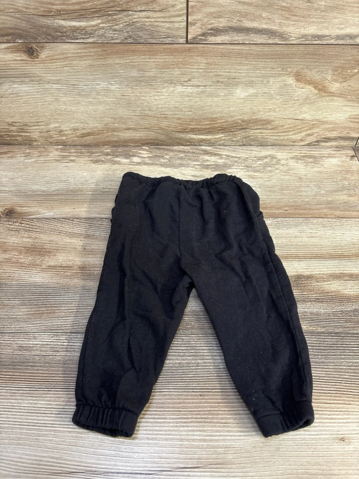Flat lay of Old Navy black joggers 12-18 months showcasing elastic waistband and cuffed ankles on wood floor