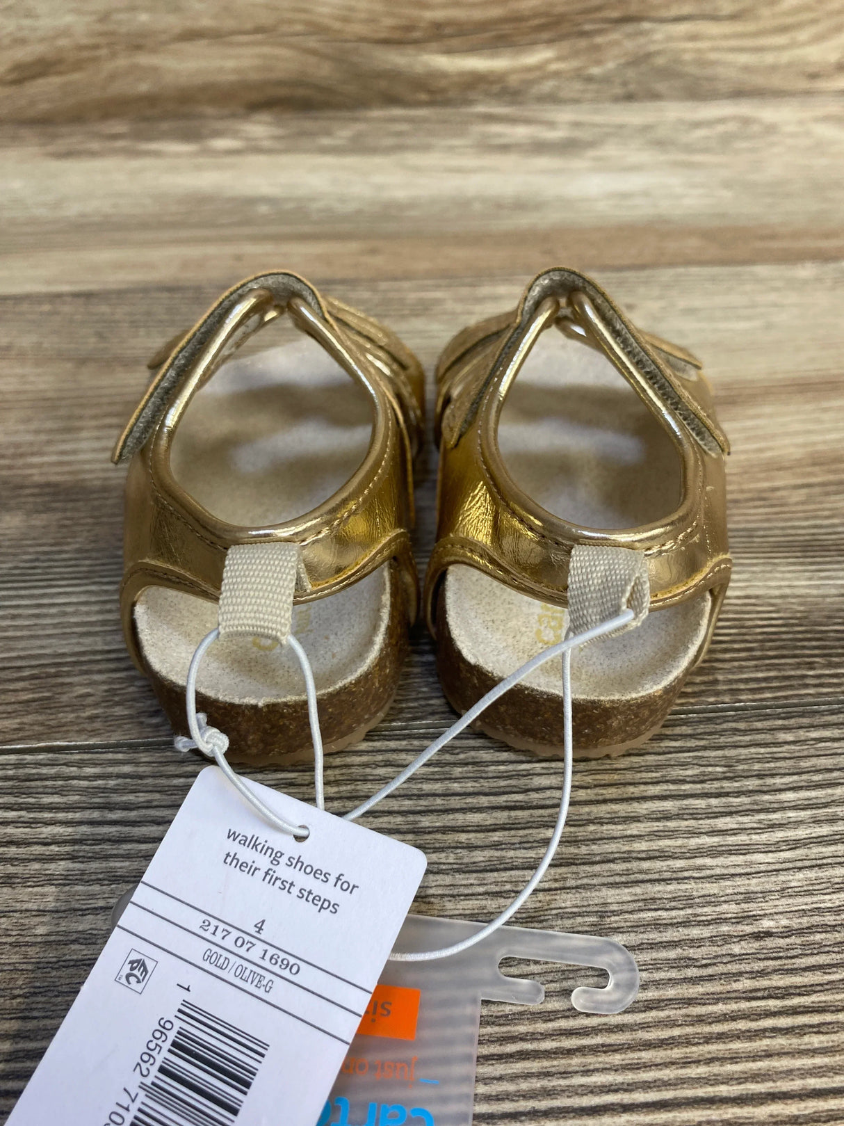 Gold toddler sandals for first steps with tags on wood background