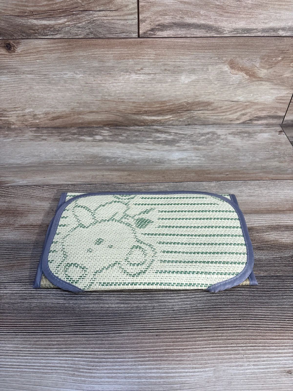 Top view of Universal Stroller Cool Seat Liner folded showing woven green giraffe pattern and gray binding on wood background
