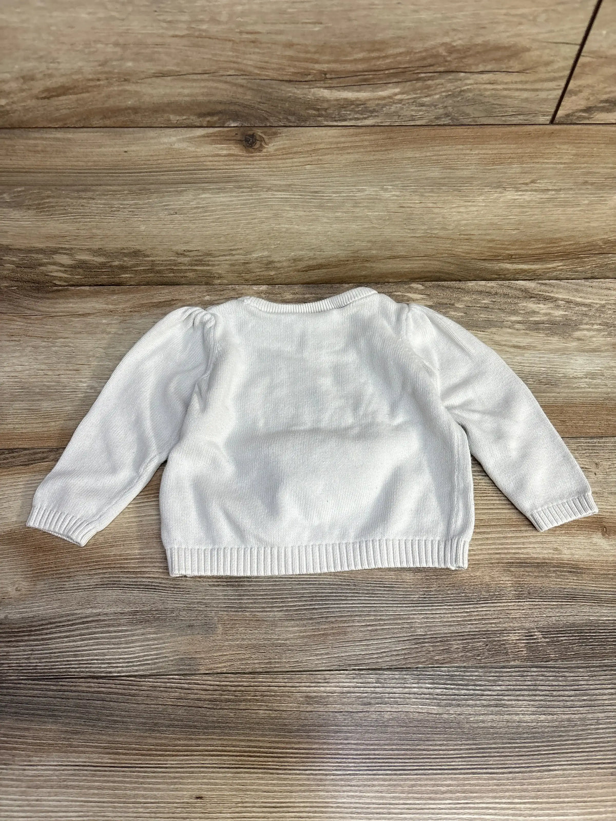White long sleeve baby sweater on wooden floor background
