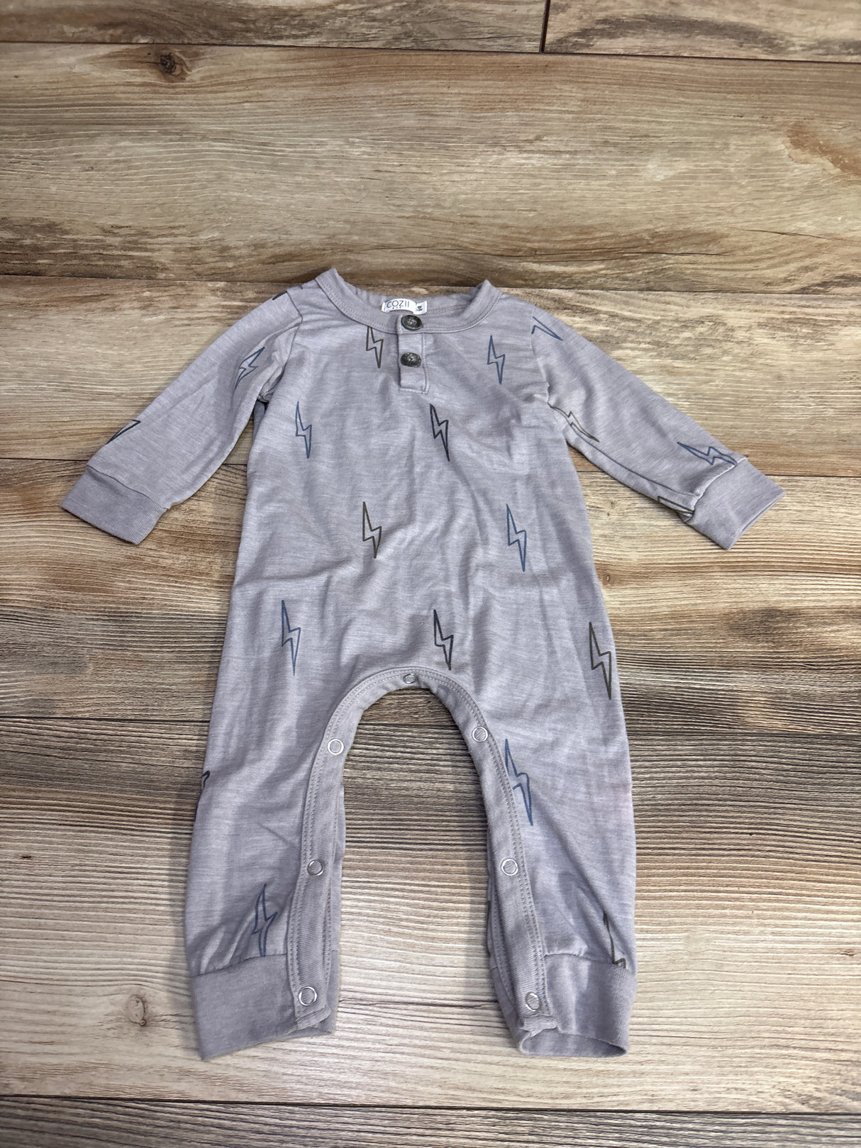 Light gray baby onesie with cloud and lightning bolt prints, long sleeves, snap buttons on legs, on wooden floor