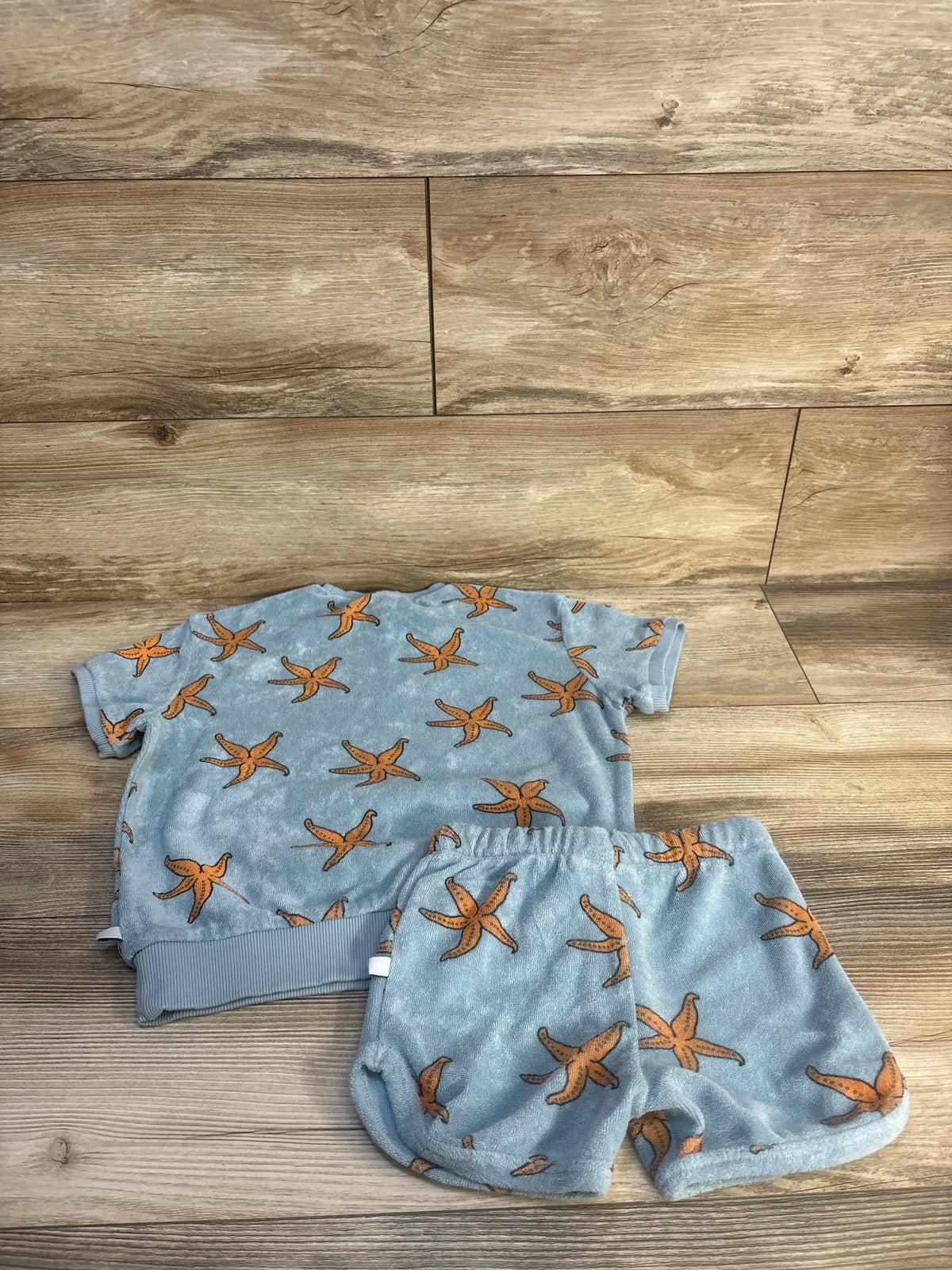Blue children's short sleeve shirt and shorts set with orange starfish print on wood background