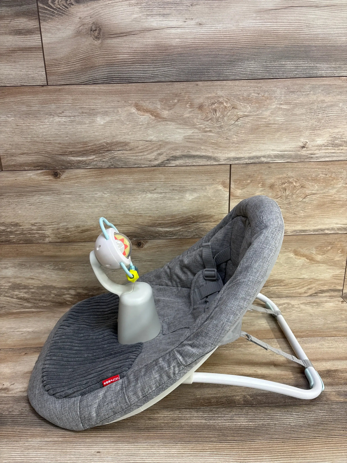 Three-quarter view of Skip Hop Silver Lining Cloud floor seat in gray with ribbed insert, harness and toy bar on wood floor