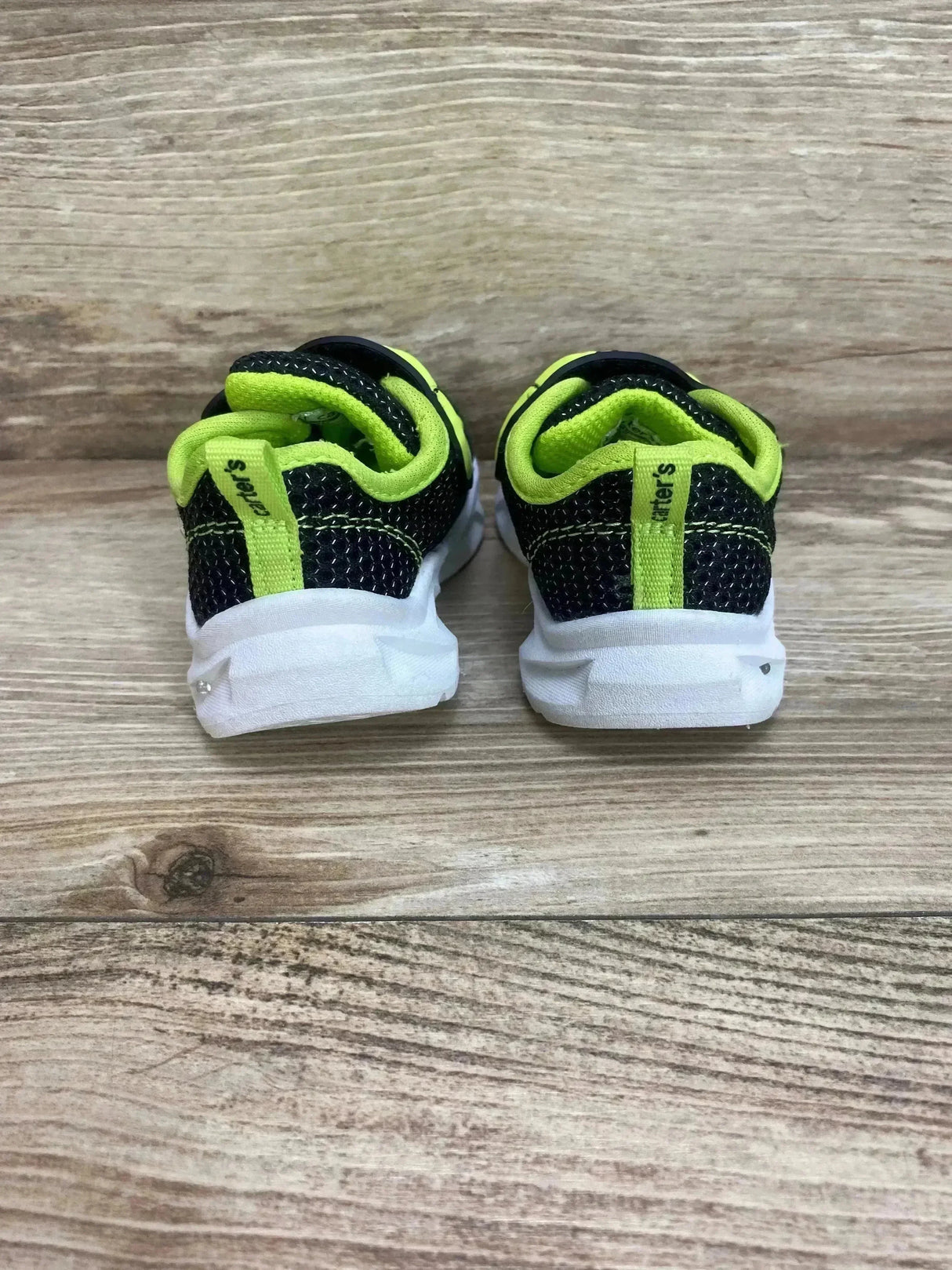 Rear view of Carter's toddler dinosaur light-up shoes, black/green, showing heel pull tabs and white light-up soles on wood
