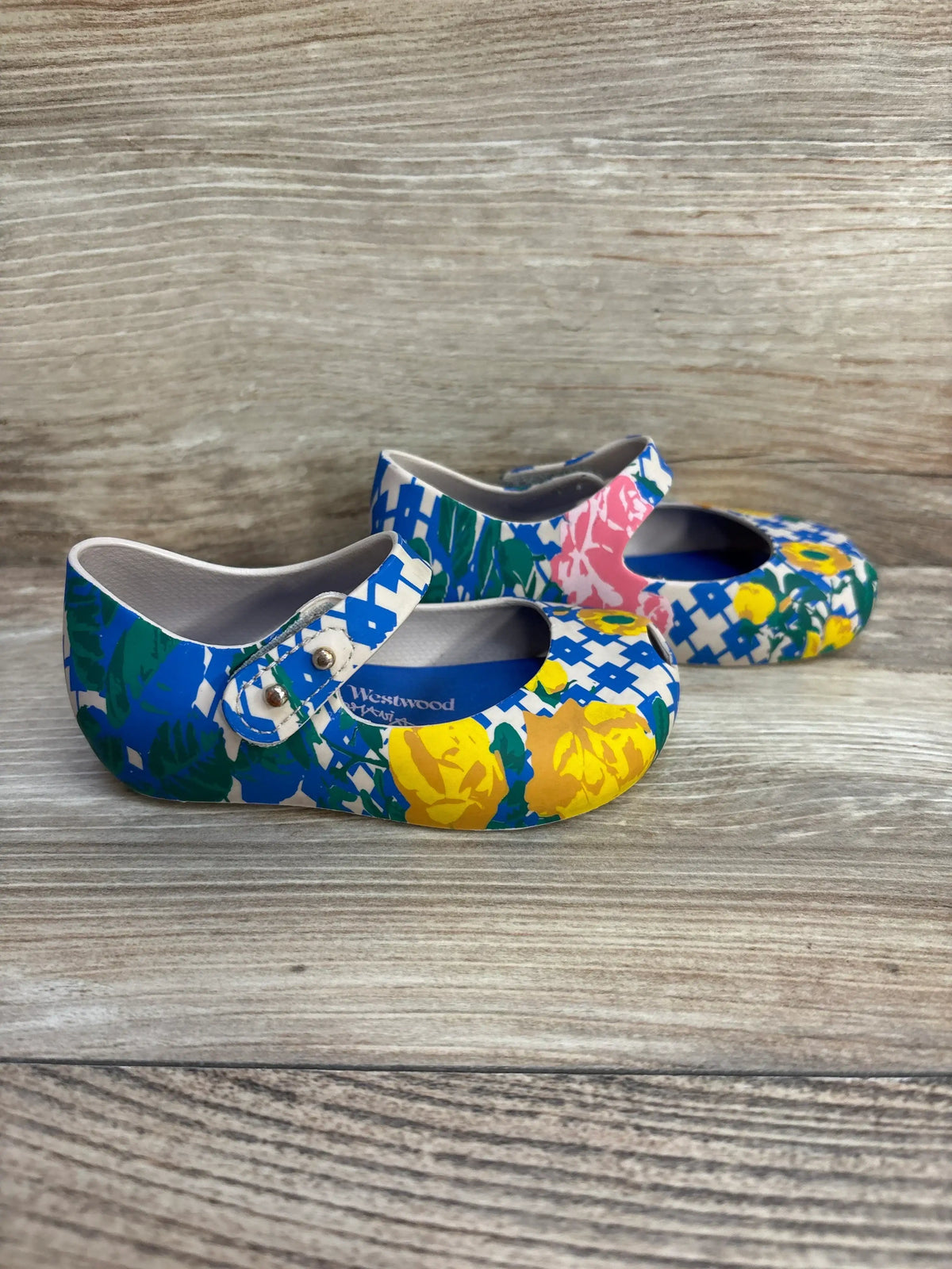 Angled side view of Vivienne Westwood girls’ Mary Jane shoes in multicolor floral print with studded strap on light wood background