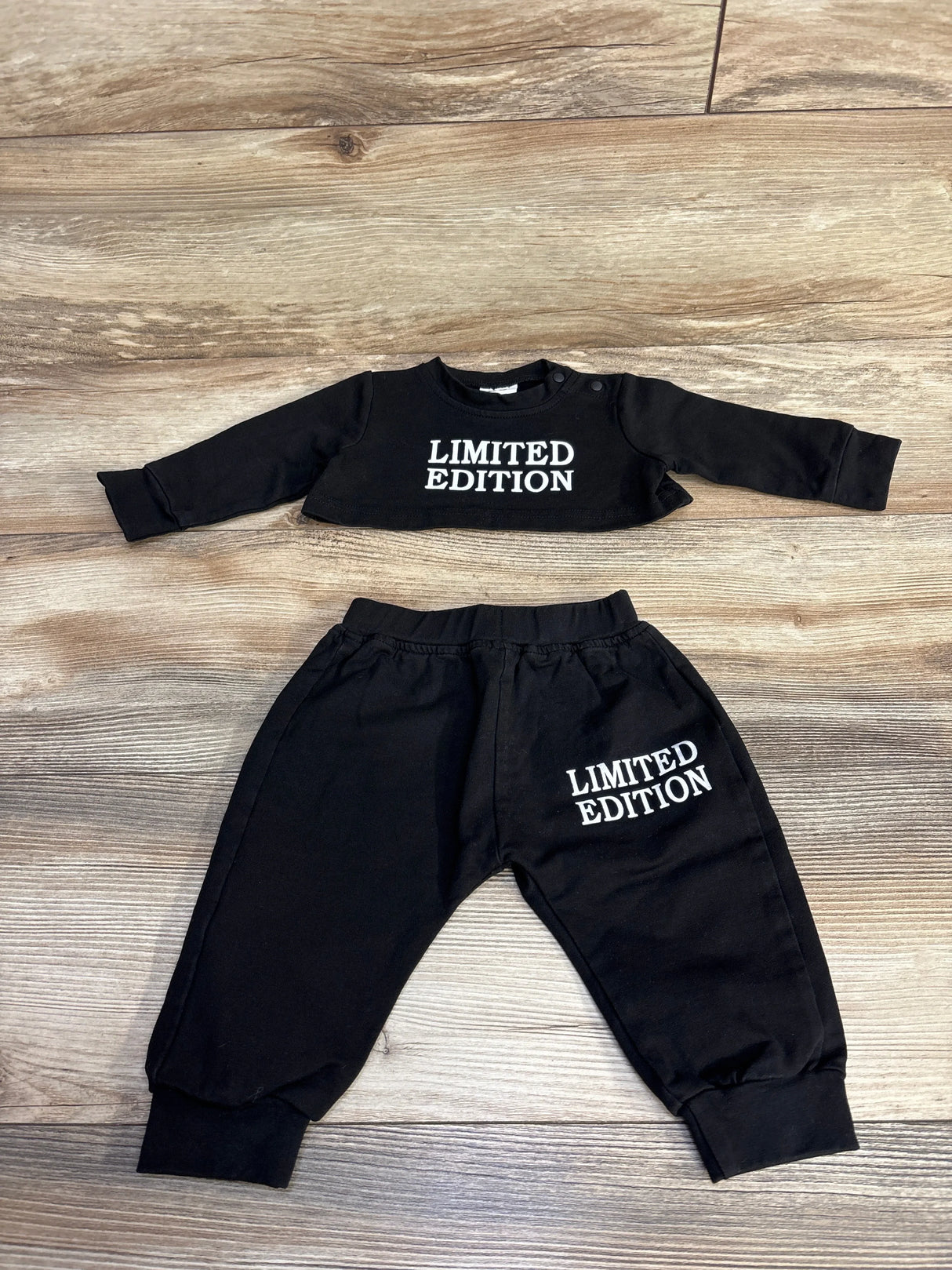 Flat lay of black 2 piece crop top and joggers showing white LIMITED EDITION text on chest and left thigh on wood background