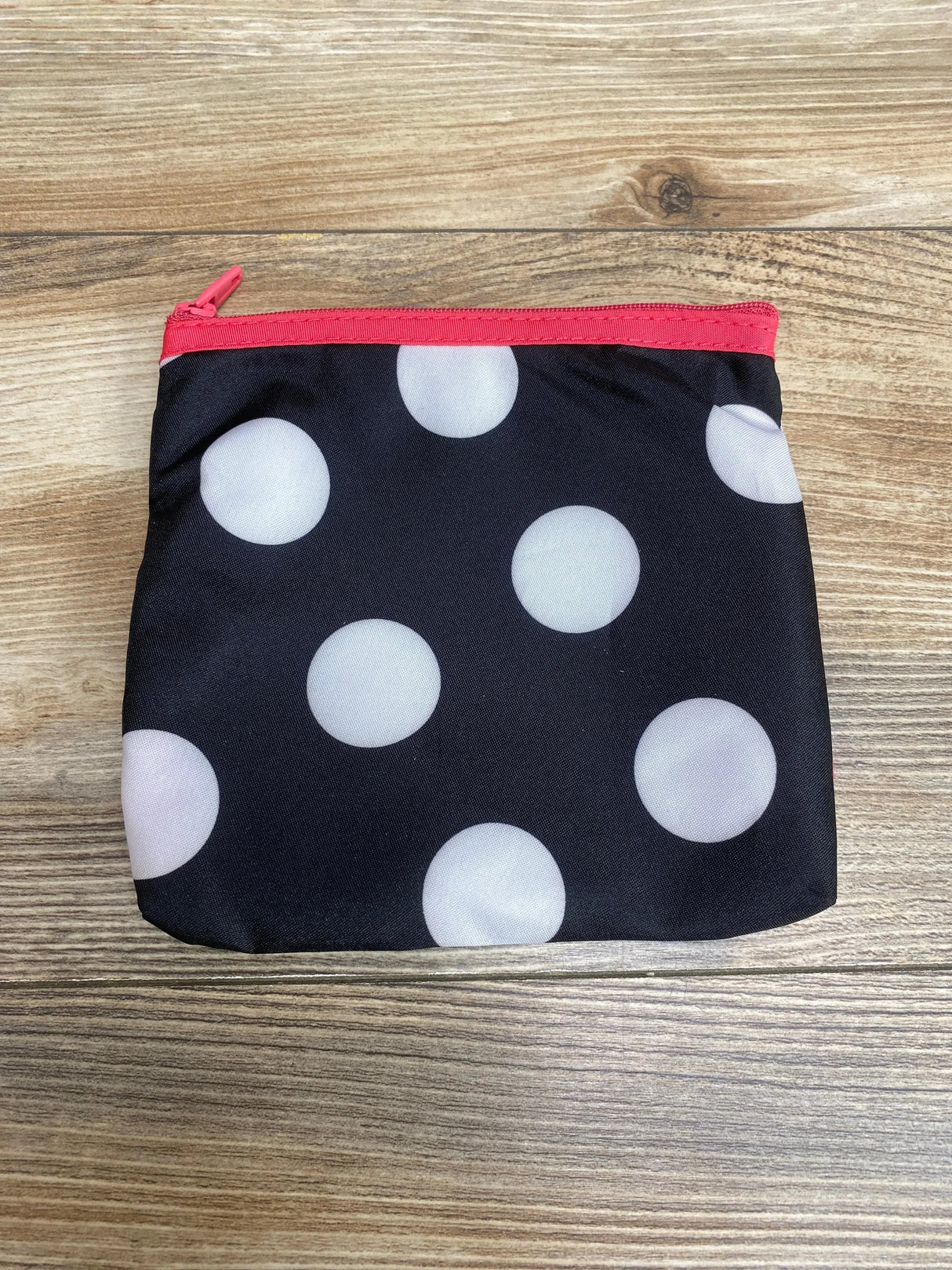 Top-down of Minnie Mouse zip carrying case showcasing black fabric with white polka dots and pink zipper on wood surface