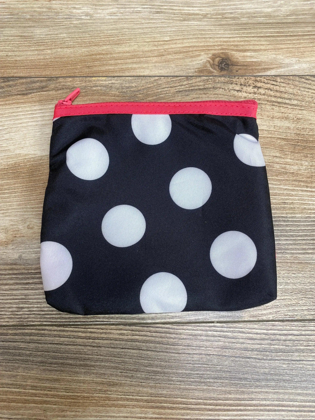 Top-down of Minnie Mouse zip carrying case showcasing black fabric with white polka dots and pink zipper on wood surface