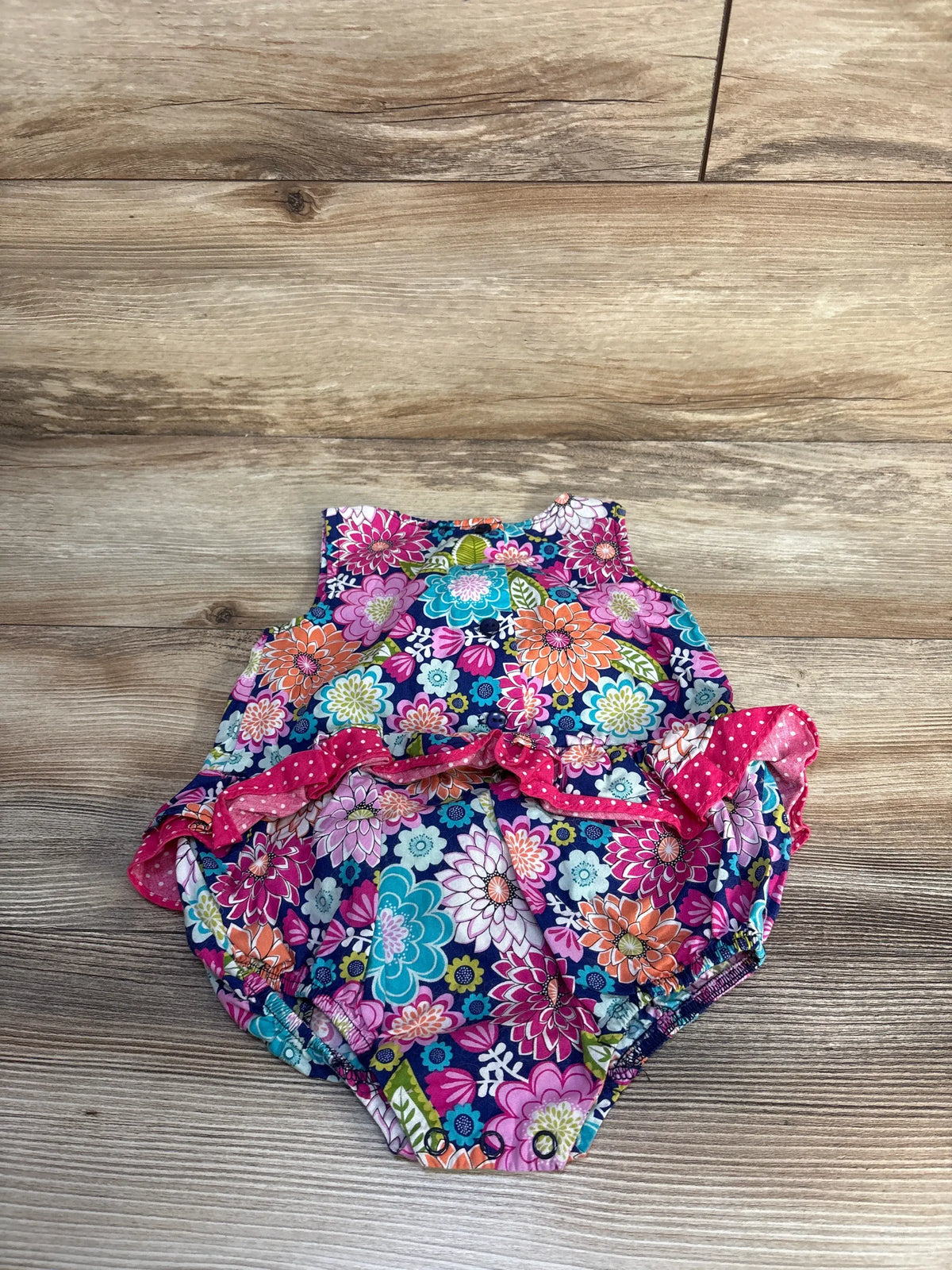 Flat front view of Bonnie Baby floral bubble romper showcasing multicolor floral print and gathered legs on a wood floor
