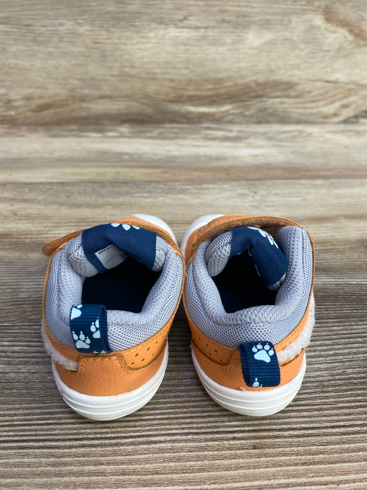 Pair of small orange baby shoes with white soles, grey mesh lining, and blue paw print pull tabs
