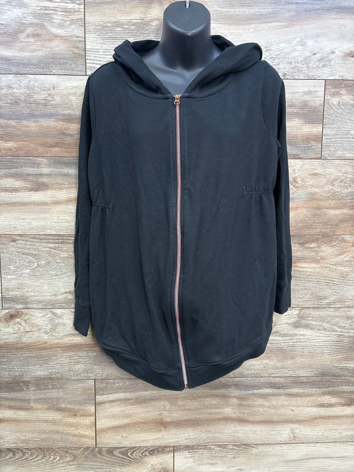 Black zip-up maternity hoodie with hood, displayed on mannequin against wood panel background