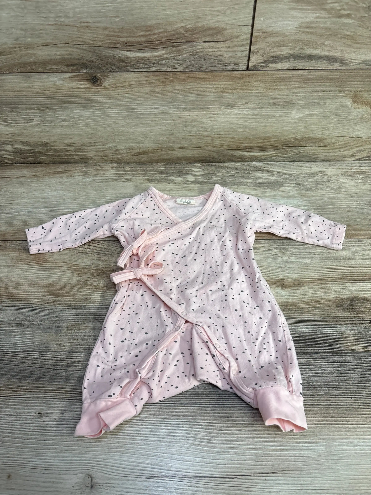 Light pink baby kimono onesie with black speckled pattern and tie closures, displayed on wooden floor