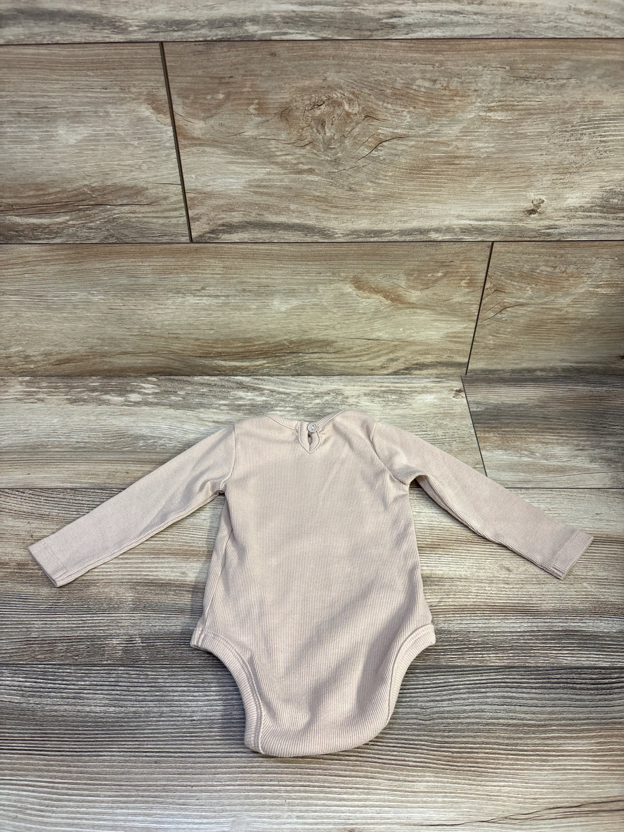 Flat lay of ribbed long-sleeve baby bodysuit size 6-9 months showing back button closure, beige on wood background