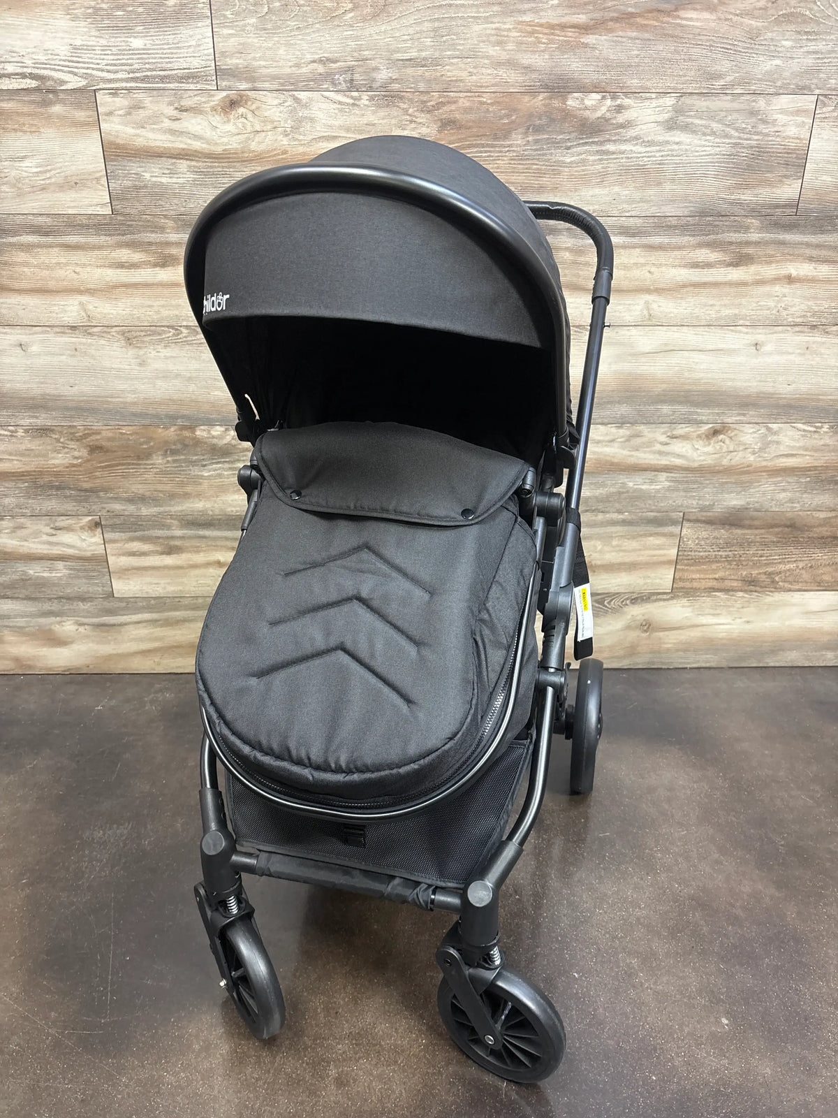 Front view of Cochilder Lite 2.0 stroller with footmuff showcasing black finish and canopy with wood-patterned background
