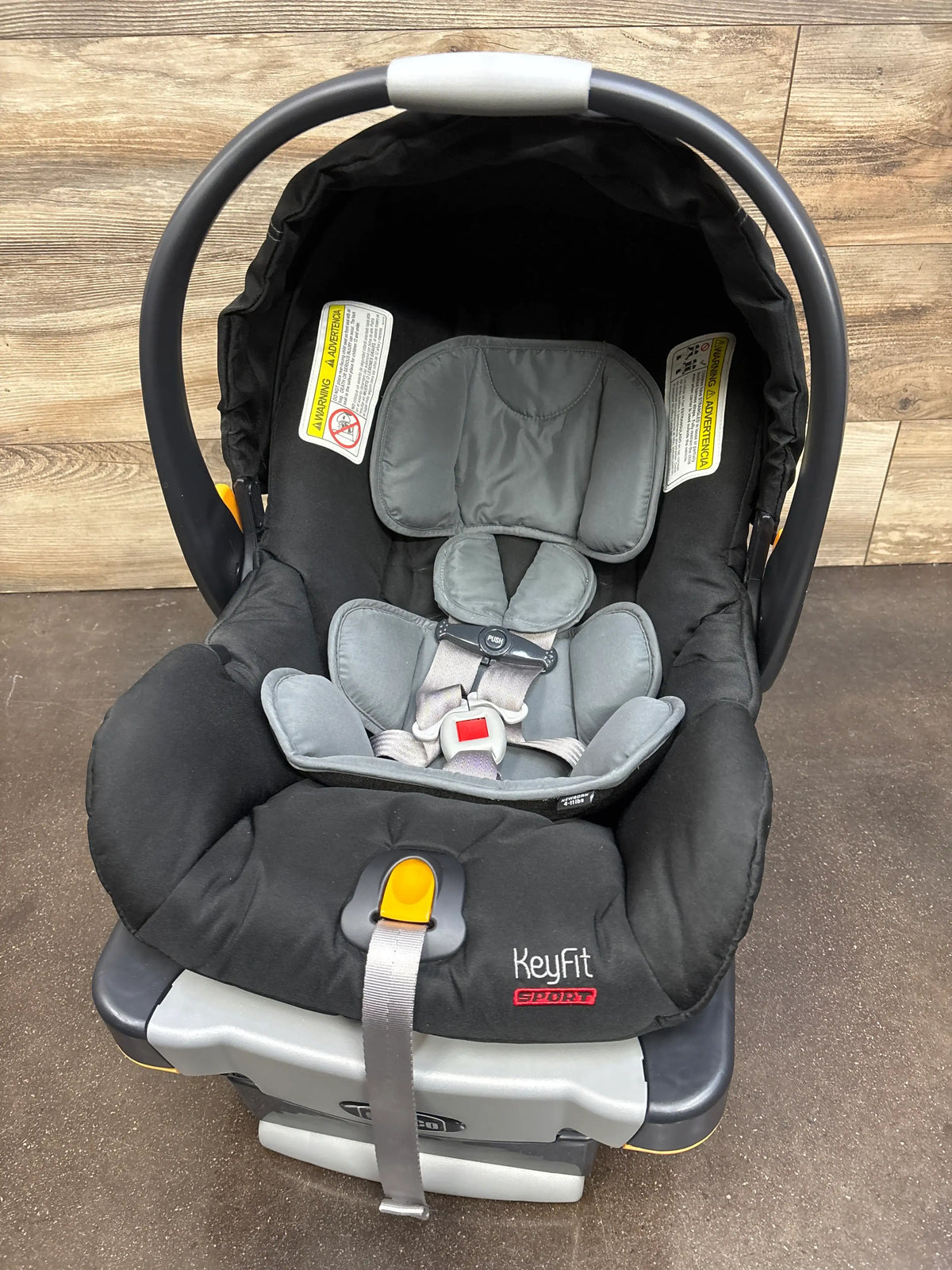 Front view of Chicco KeyFit infant car seat in Encore showcasing gray padding and five point harness with wood floor background