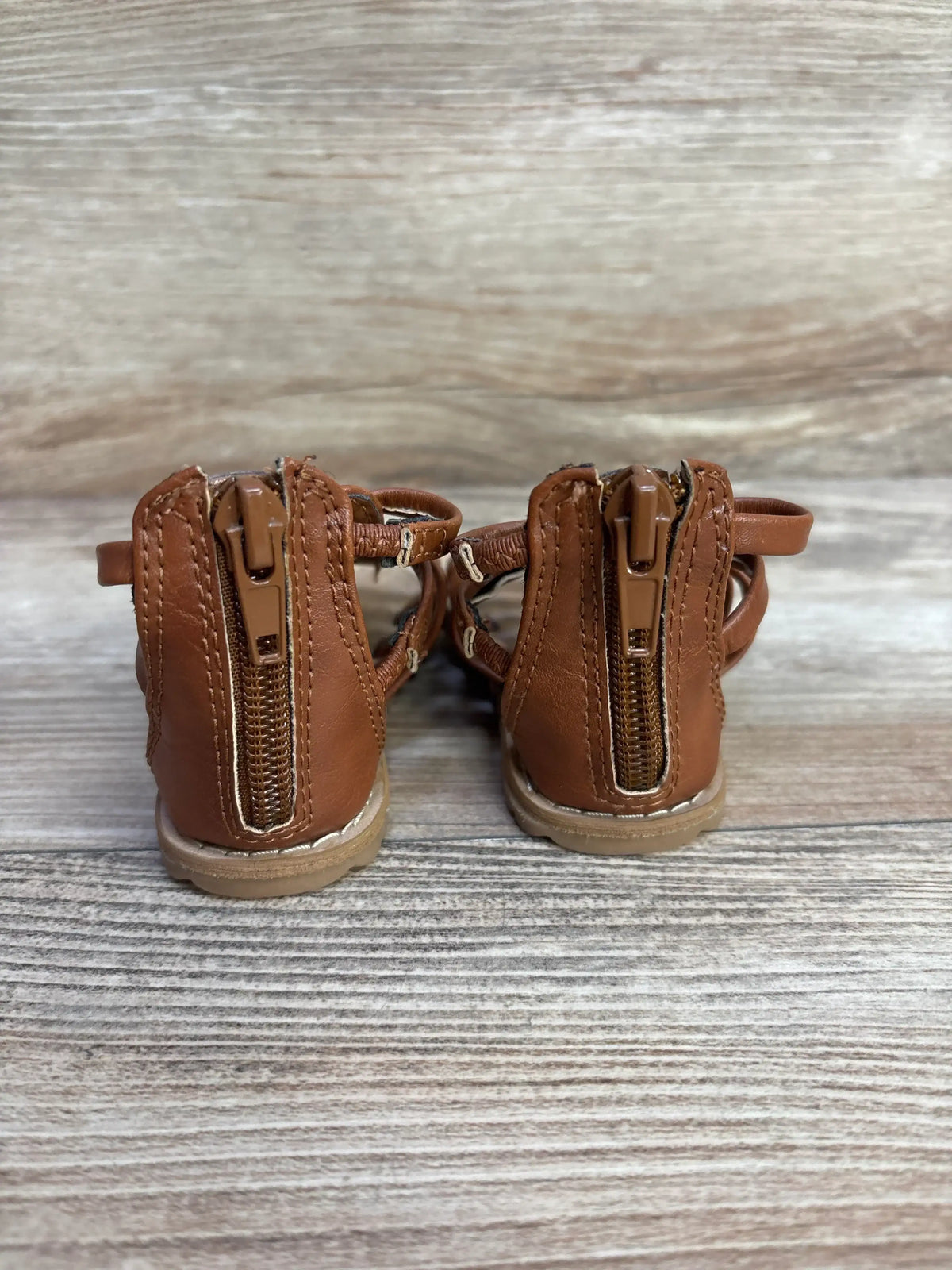 Rear view of Wonder Nation toddler gladiator sandals in brown showing back zipper closure and stitched sole on wood background