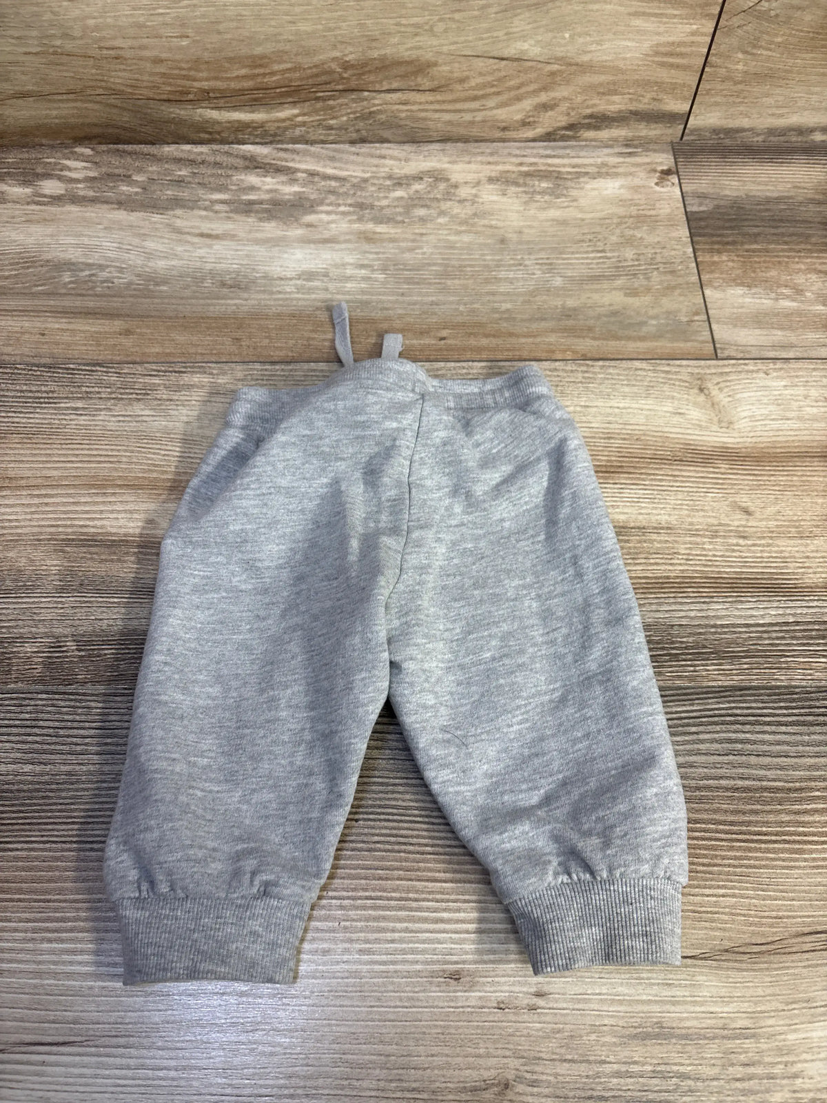 Front view of H&M drawstring joggers showcasing soft grey color, drawstring waist, and cuffed ankles on a wood floor