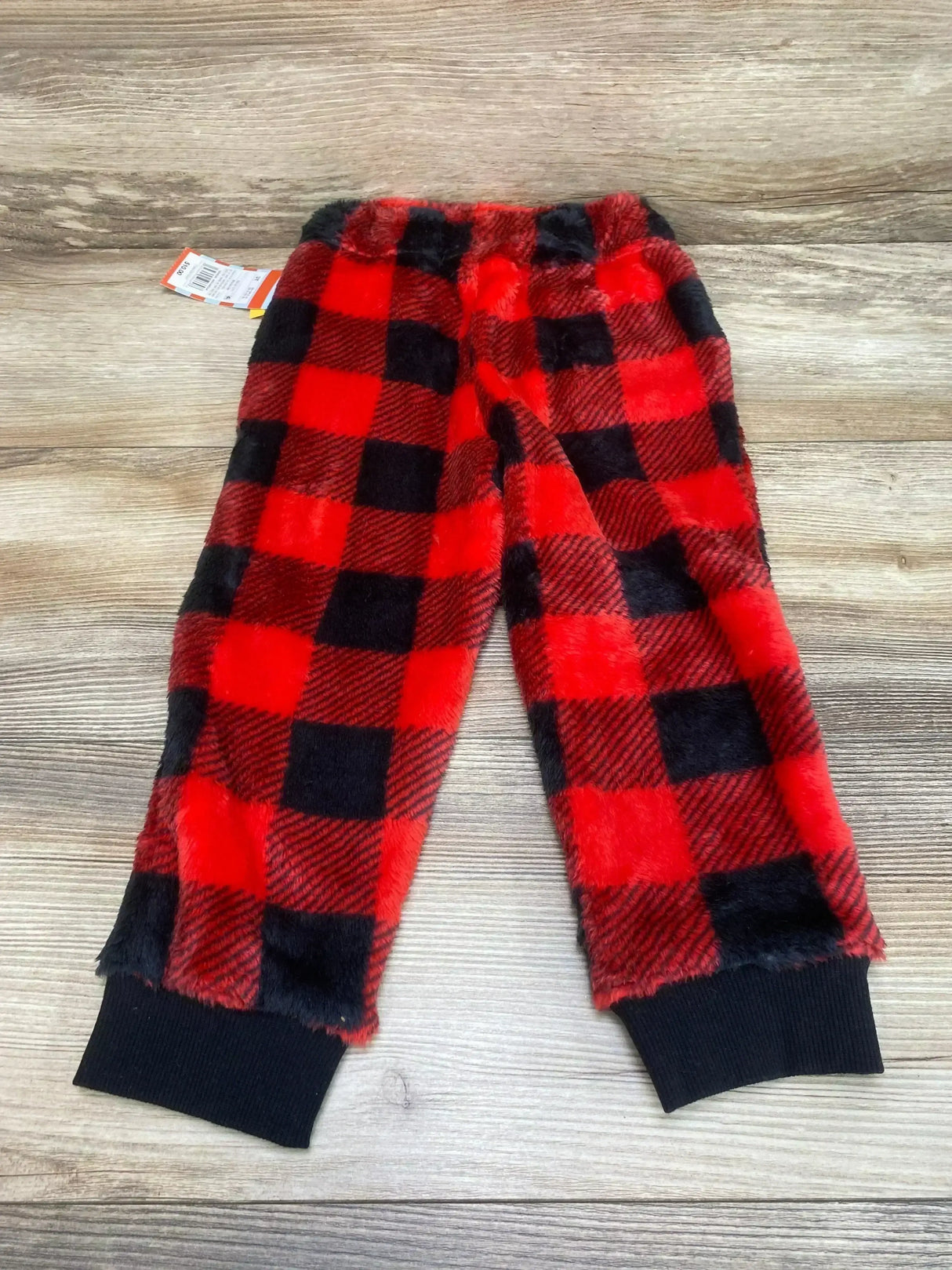 Front flat lay of toddler red and black buffalo plaid cozy pants with fleece, elastic waist and black ribbed cuffs on wood