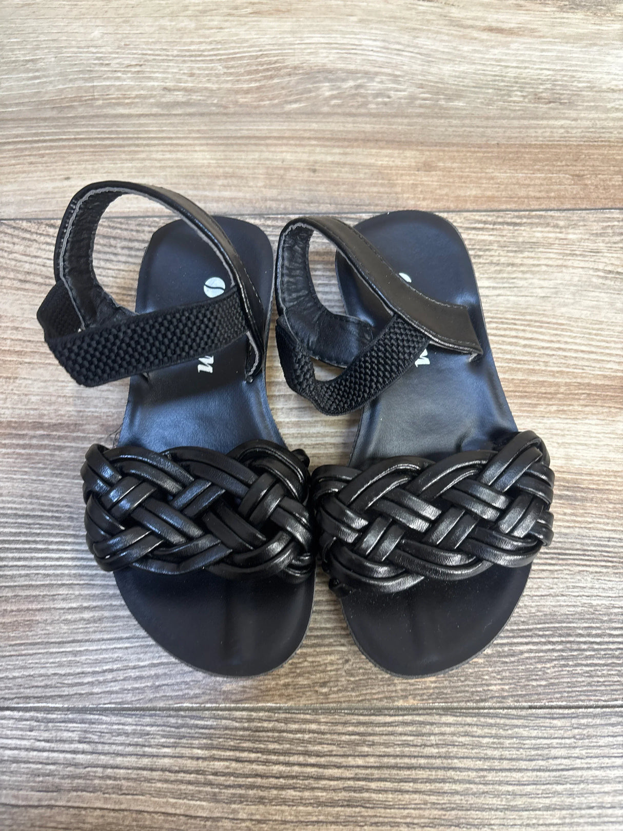 Black woven strap toddler sandals with ankle velcro on wood floor