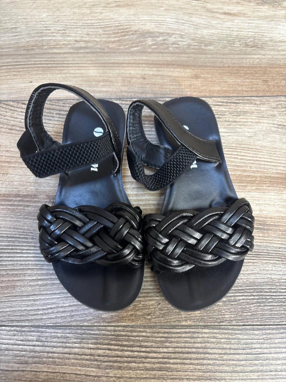 Black woven strap toddler sandals with ankle velcro on wood floor