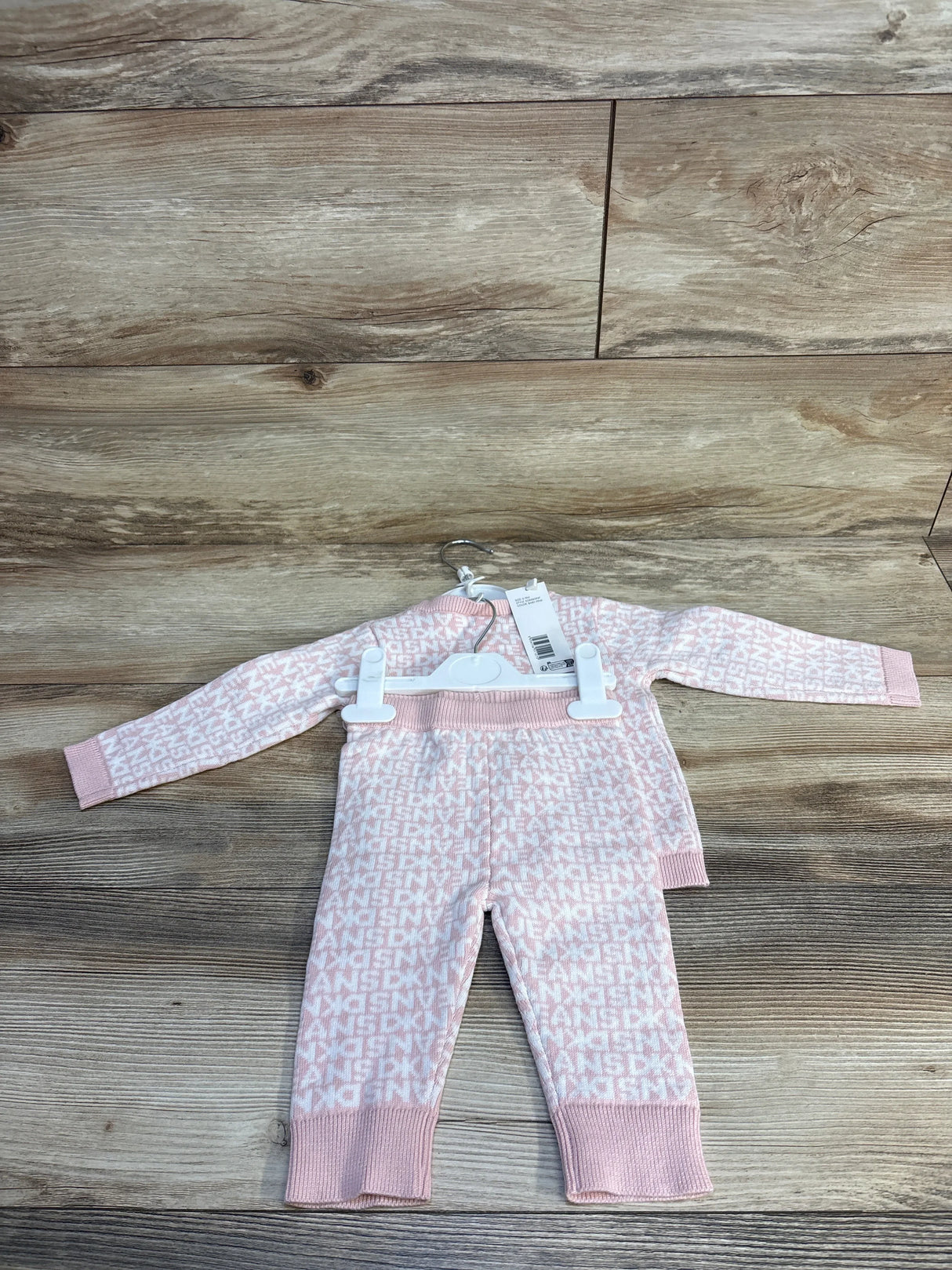 Front view of DKNY baby knit cardigan and pants in baby pink showing logo jacquard, button front and ribbed cuffs on wood
