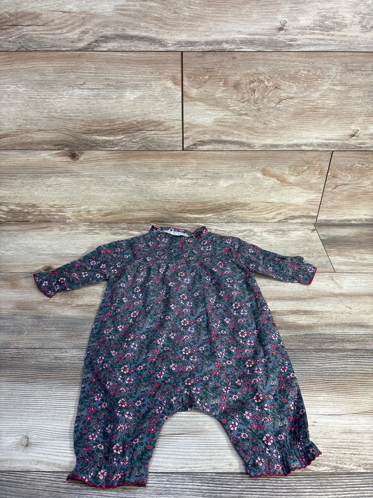 Front view of Petite Plume Madeline romper showcasing its blue floral print, long sleeves, and ruffled cuffs on a wood floor