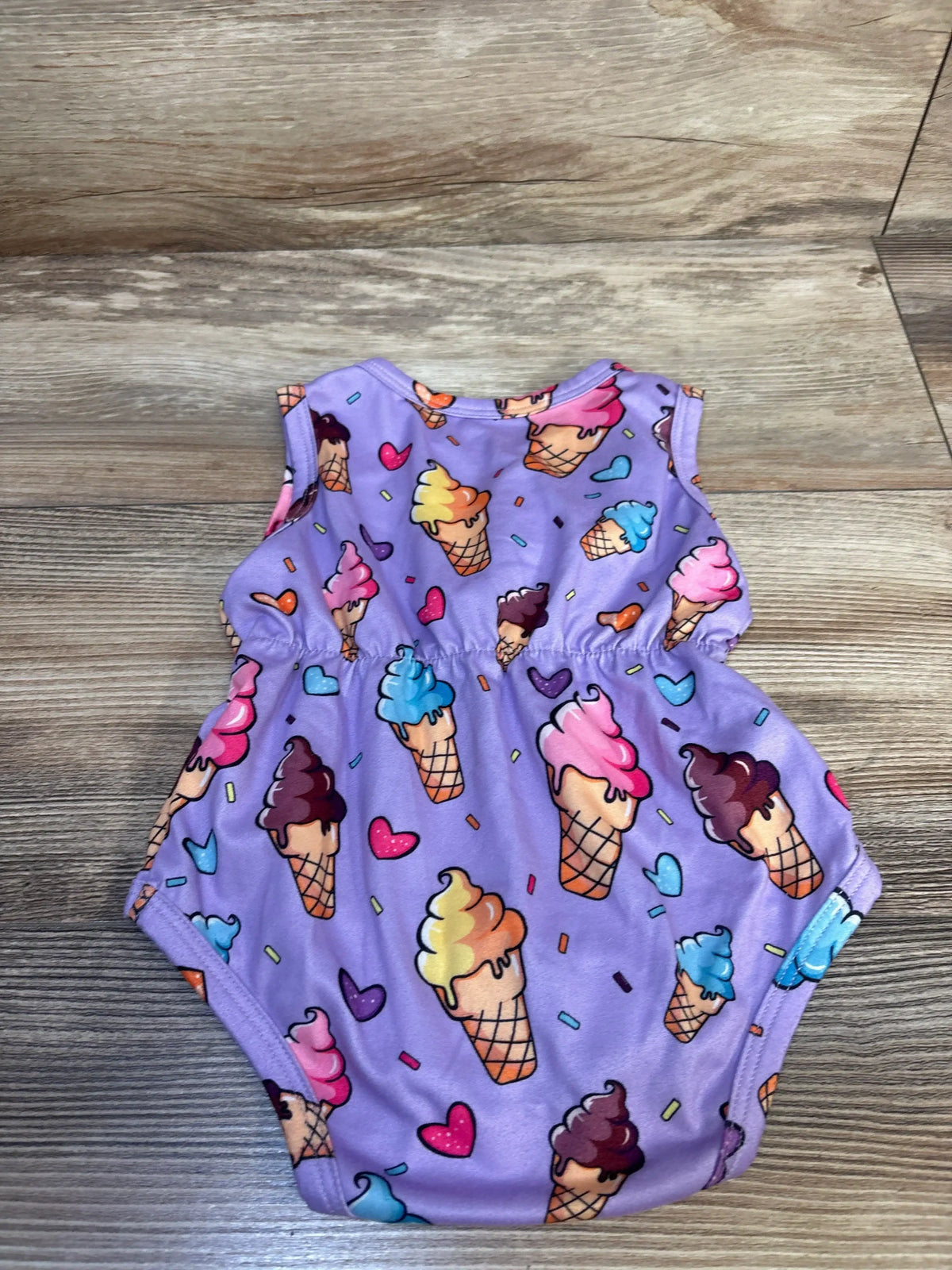 Flat lay of purple baby tank bodysuit with ice cream and heart print, sleeveless, gathered waist on wood background