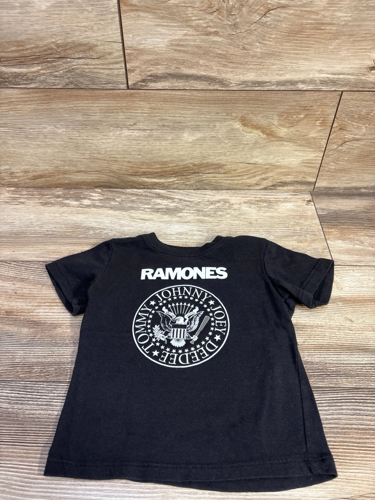 Flat lay of toddler black Ramones T-shirt showcasing white band logo and crew neck with wood floor background