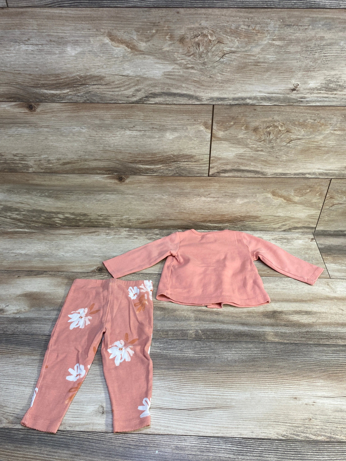 Flat lay of Carter’s 2pc pink button-top and floral leggings set, back of top and leggings on wood background