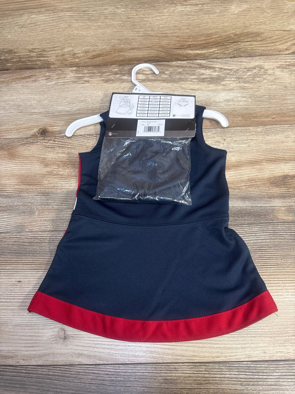Navy blue and red sleeveless baby dress on white hanger with attached packaging on wooden background
