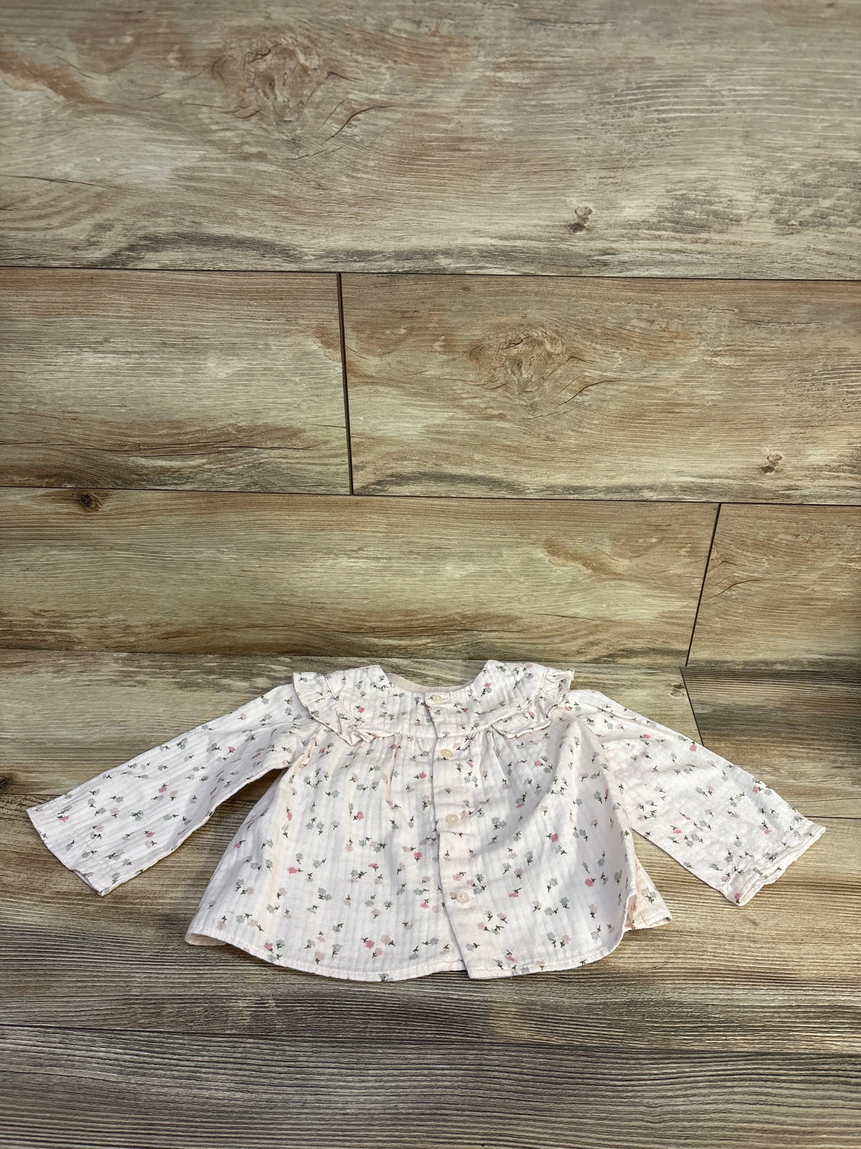 Baby girl floral blouse with ruffled collar, soft pastel print, long sleeves, laid on wood floor
