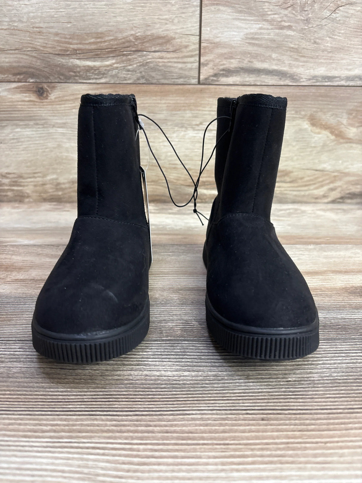 Pair of black children's winter boots with flat rubber soles on wooden floor