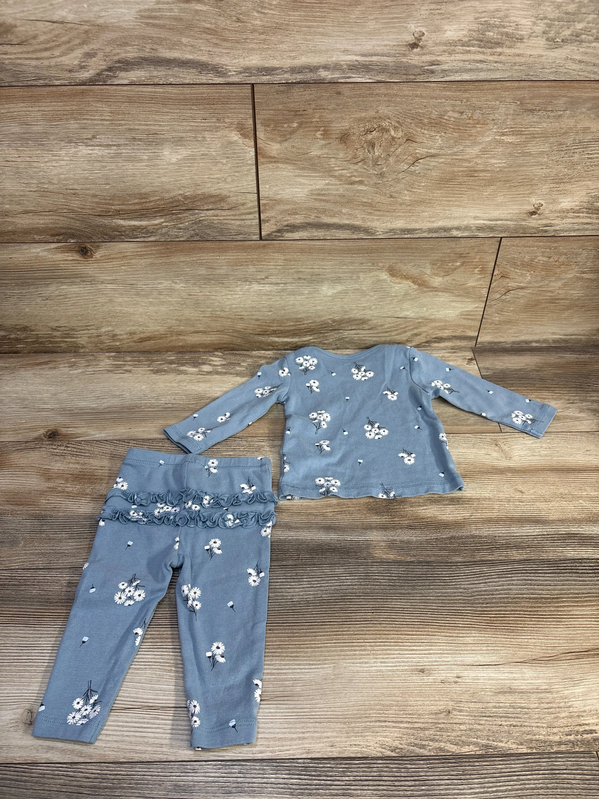 Flat lay of Carter's blue 2-piece baby set, long-sleeve floral shirt and leggings with ruffle detail on wood plank background