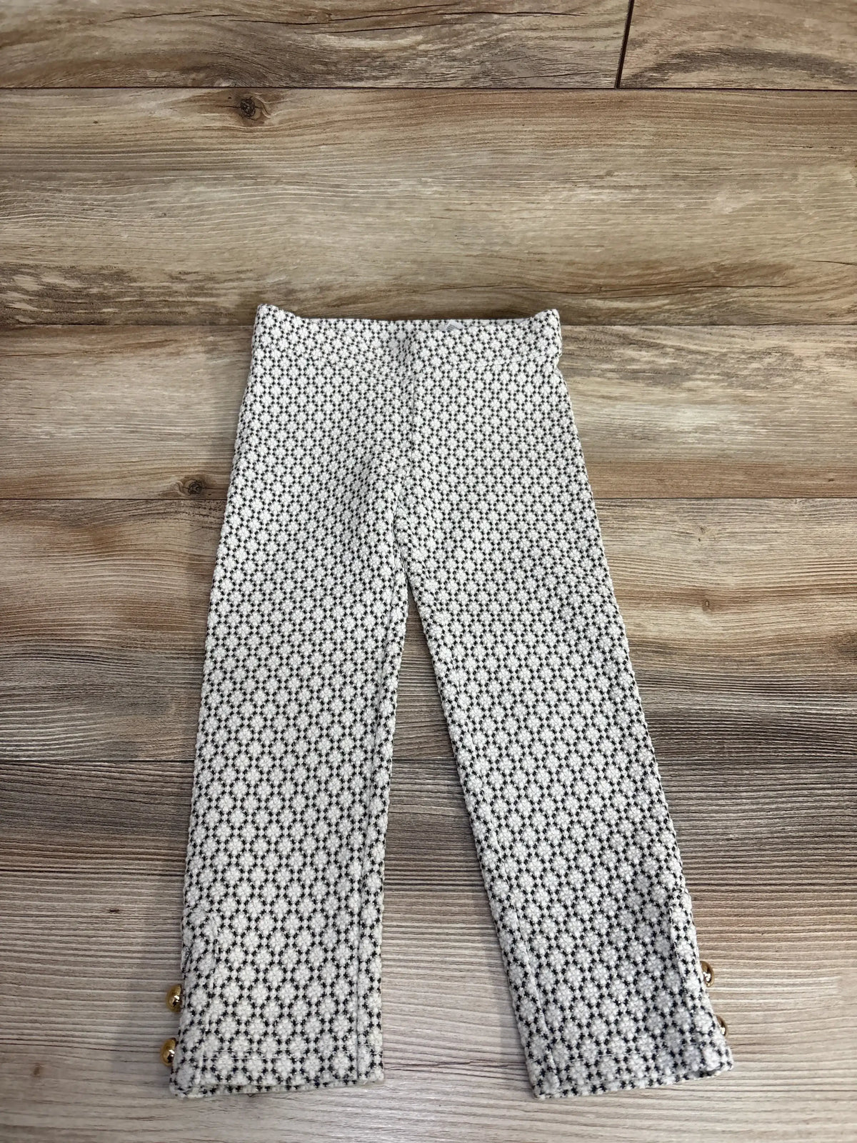 Patterned girls’ pants with black and white geometric print and decorative gold buttons