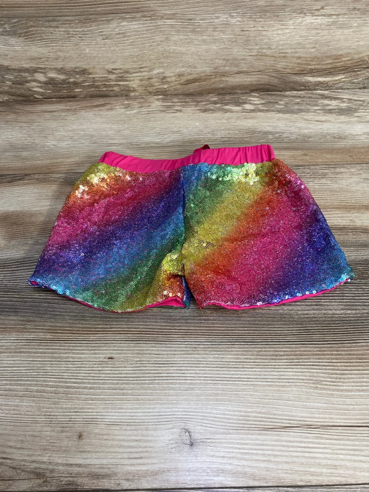 Front of toddler rainbow sequin shorts, size 4-5T, with multicolor gradient and pink elastic waistband on wood background