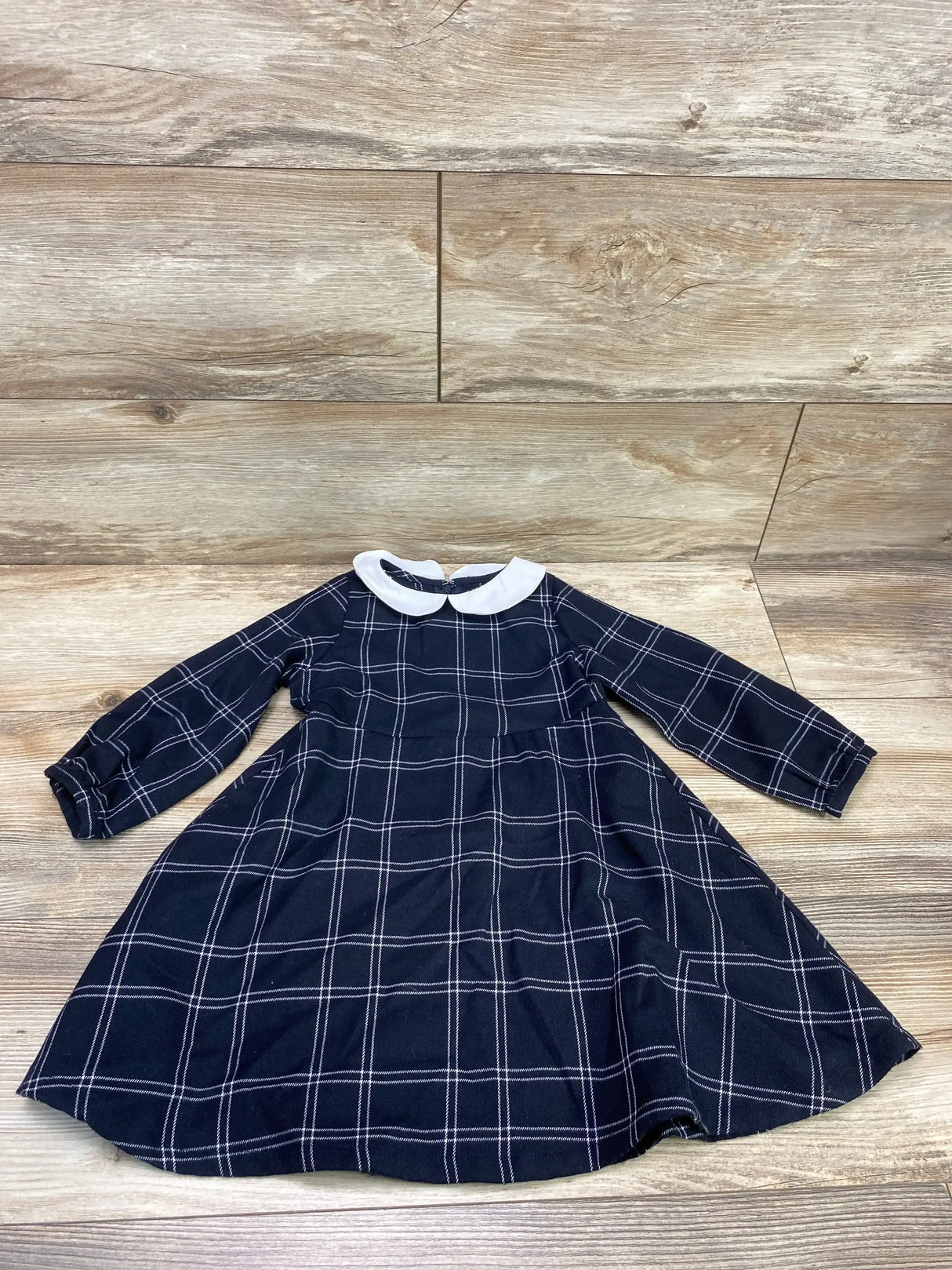 Flat lay of toddler black plaid Peter Pan collar dress size 2T showing white collar and long sleeves on wood floor