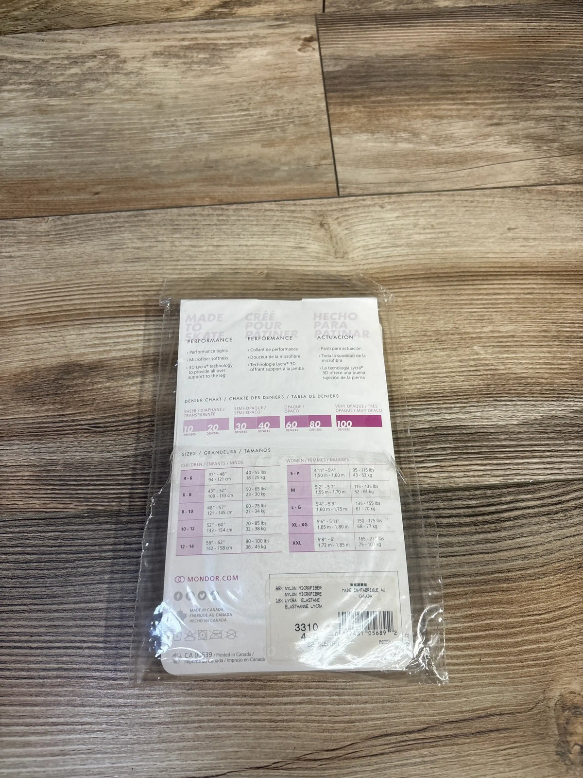 Back view of NEW Mondor Footed Skate Tights 3310 in Suntan, size 4-6, packaged with a sizing and denier chart on a wood floor