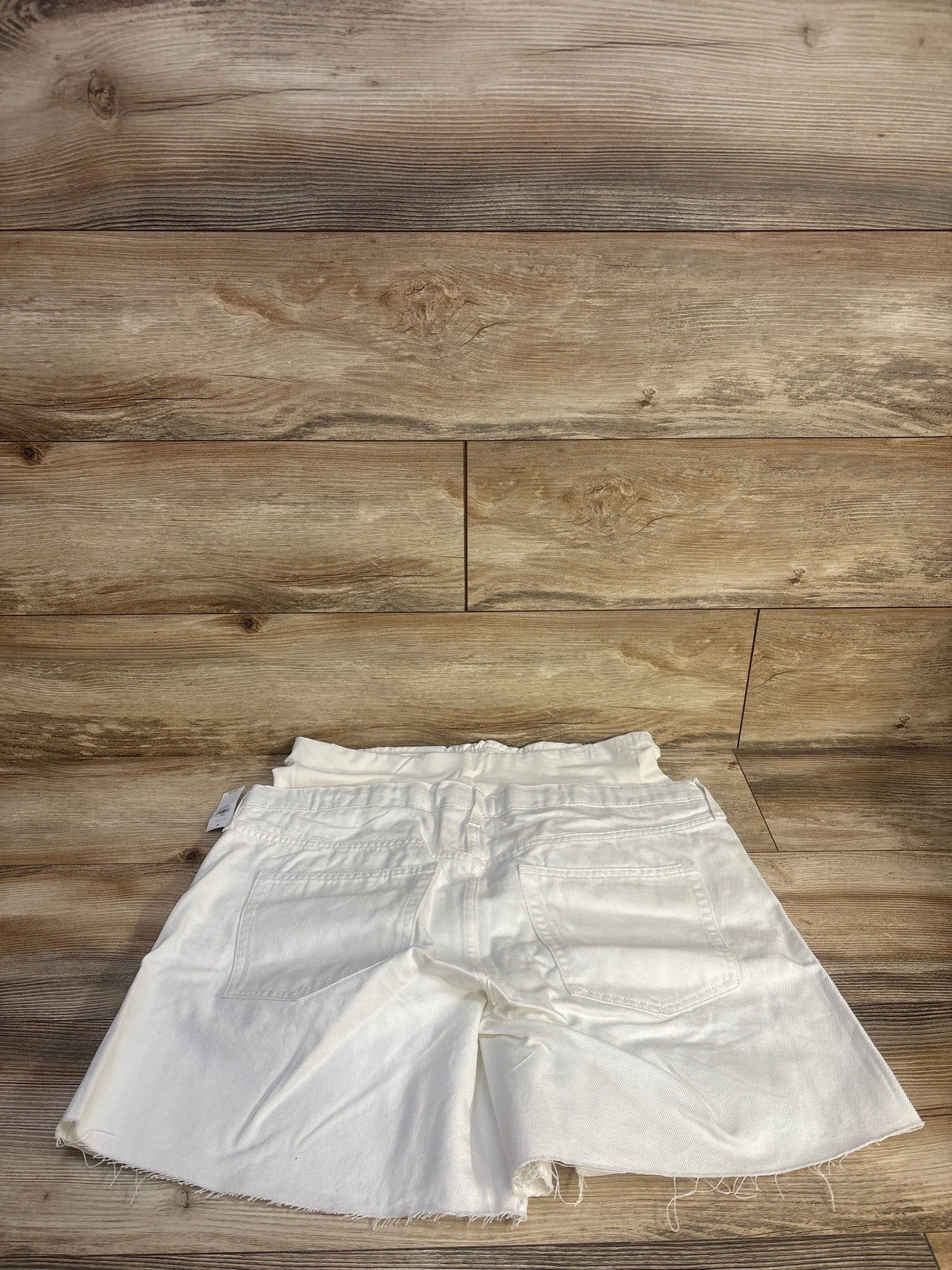 Rear view of white Gap maternity denim Bermuda shorts showcasing full-panel waistband, back pockets, and frayed hems with a wood background