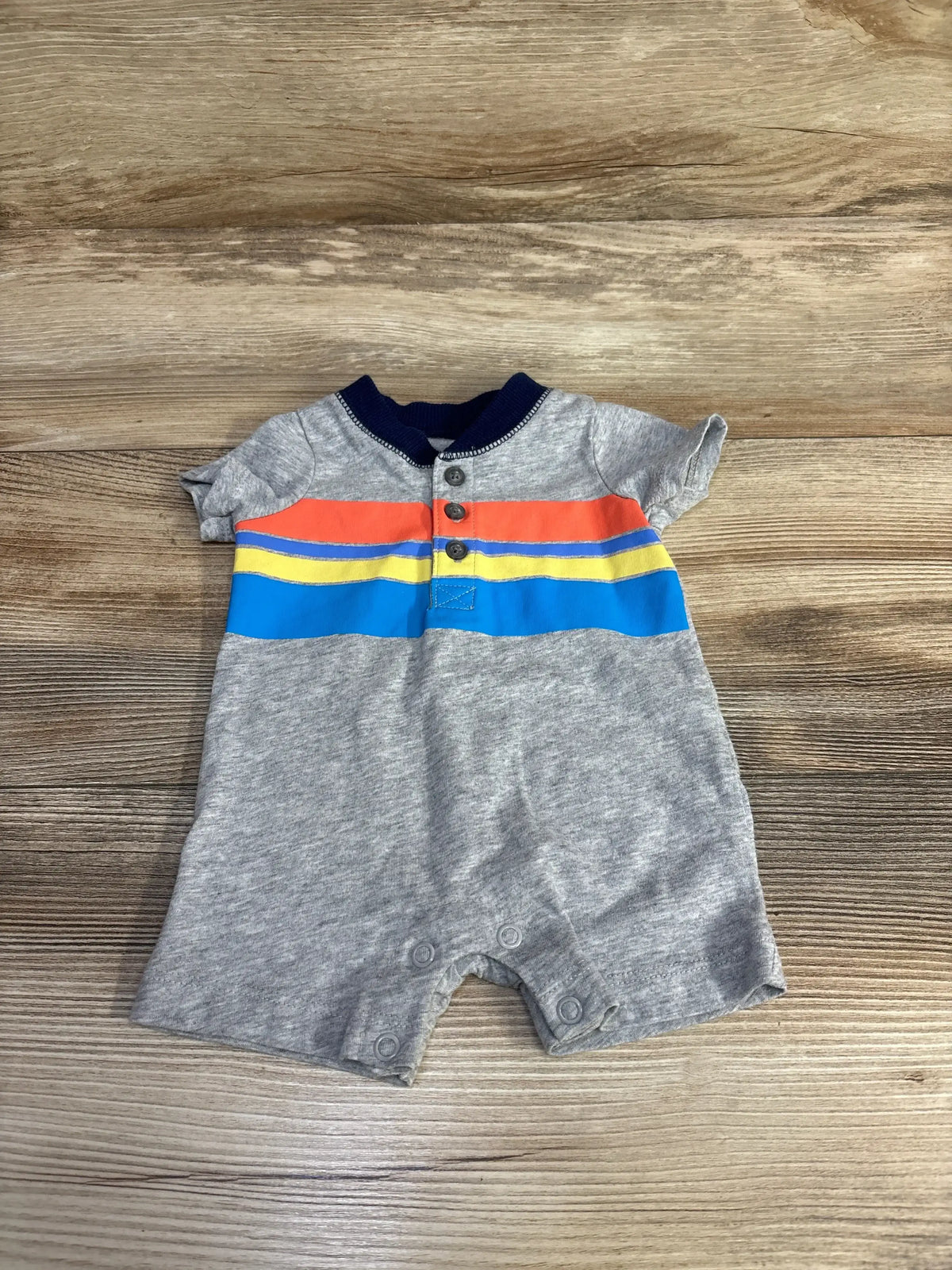 Gray baby romper with colorful stripes and buttons on wood background