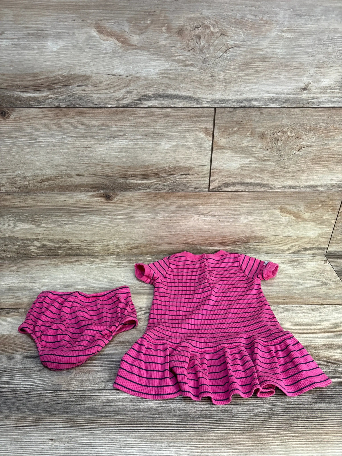 Pink striped baby dress and matching bloomers set on wood floor