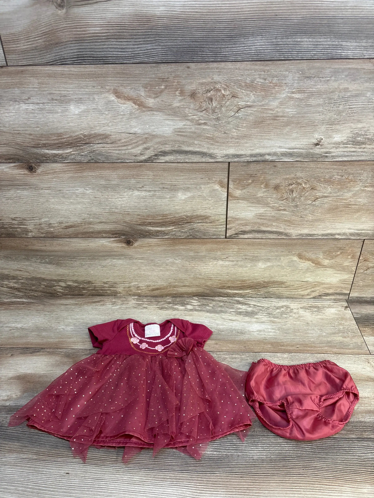 Flat lay of Princess Rose tulle dress and bloomers showcasing glitter skirt, embroidered neckline and bow on wooden background