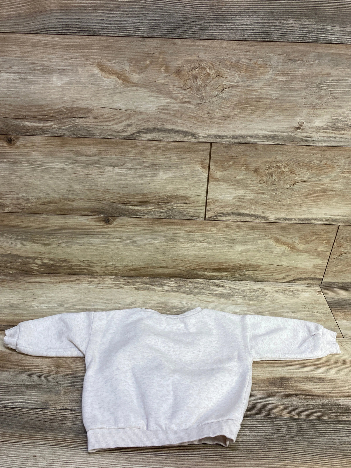 Top view of Nike ivory pullover sweatshirt with long sleeves and ribbed cuffs on a wood plank background