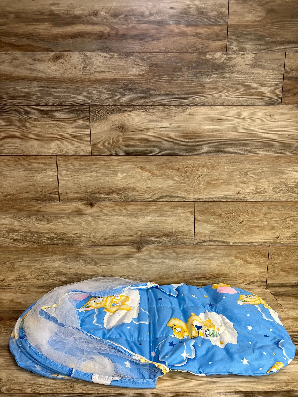 Front view of Care Bare nap mat with pillow showcasing white mesh mosquito net and blue bear-print mattress on wooden floor