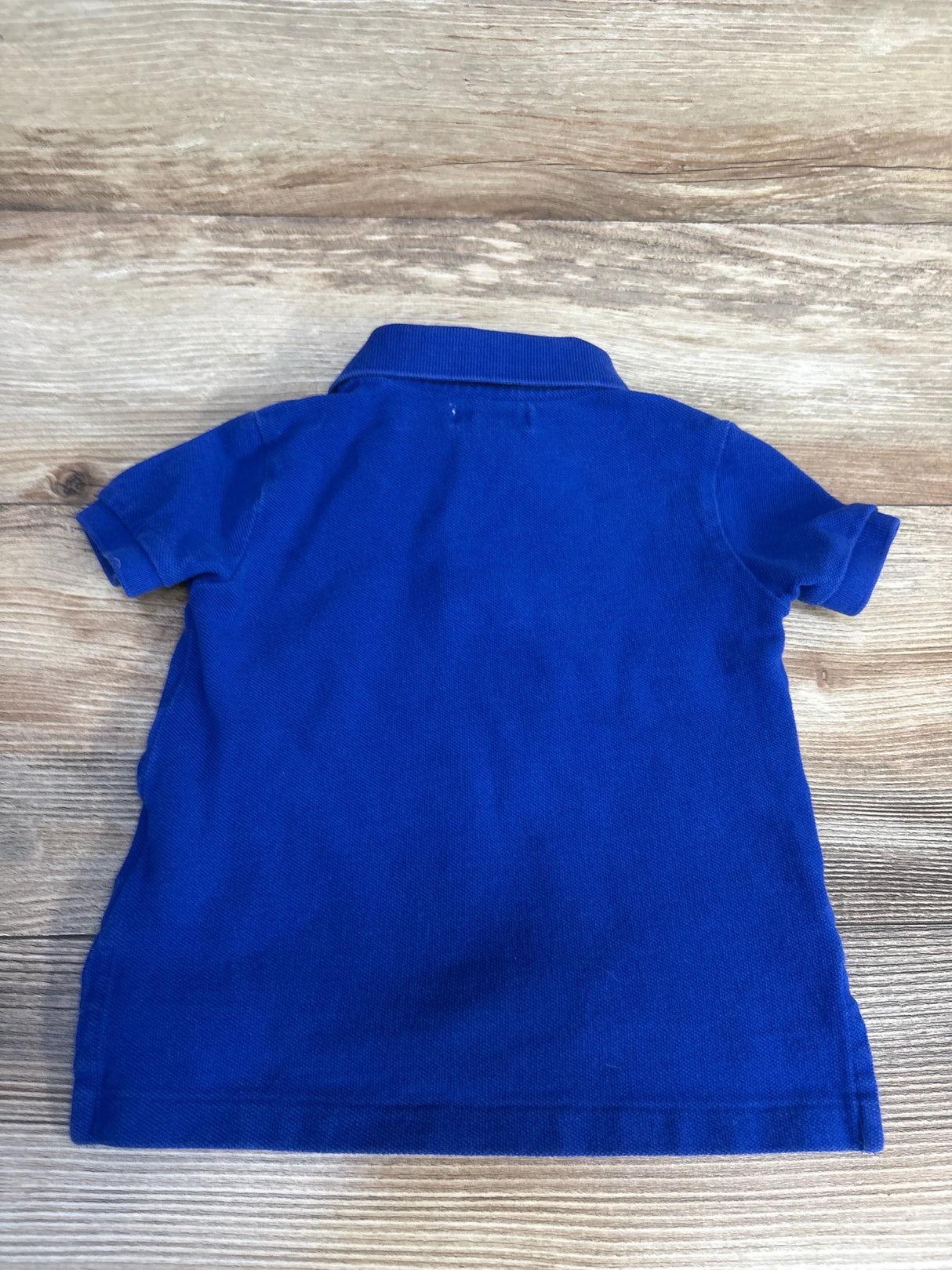 Blue kids polo shirt for toddler boys, short sleeve, solid color, laid flat on wood