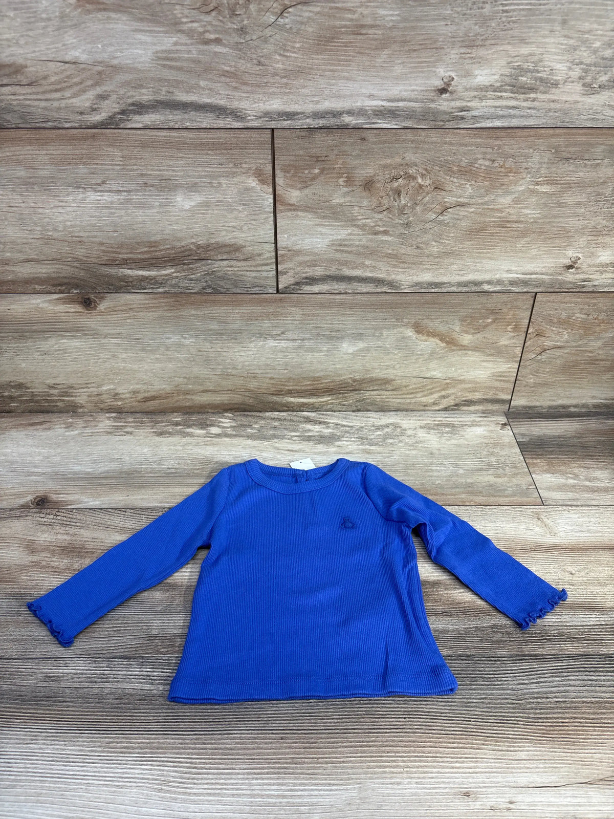 Front view of a blue Baby Gap ribbed long sleeve shirt showcasing lettuce trim sleeves on a wood floor