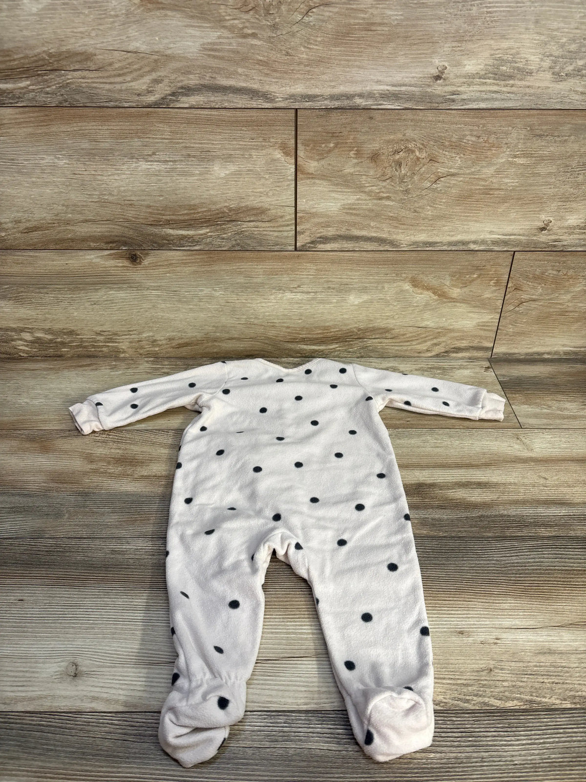 Front view of H&M beige polka dot sleeper showcasing long sleeves and enclosed feet on a wood background