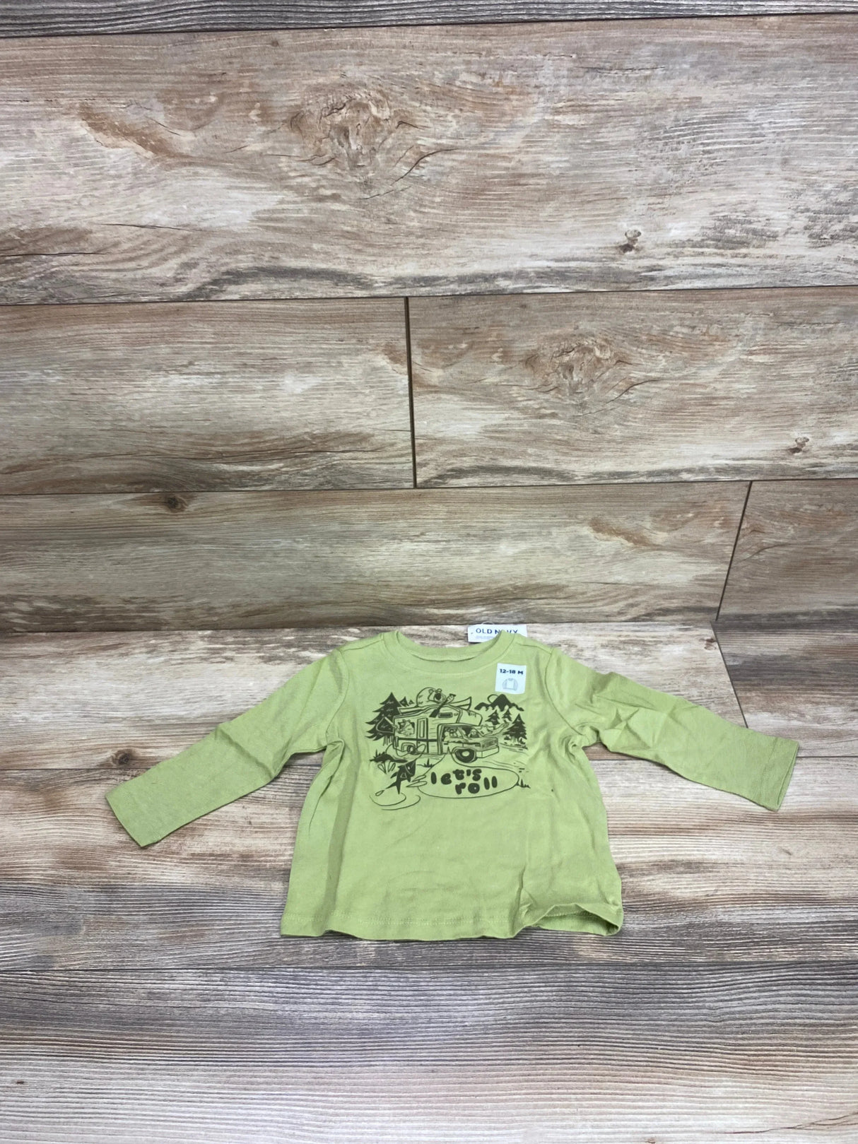 Flat lay of Old Navy toddler long-sleeve green shirt showcasing camper van lets roll graphic on wood floor background
