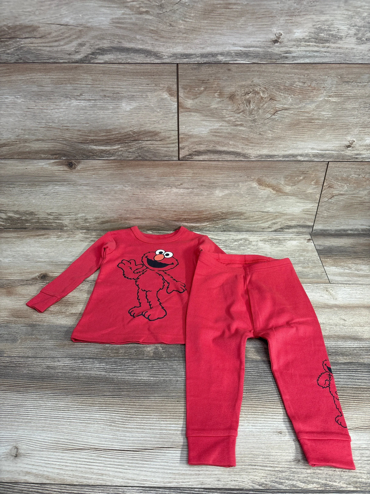 Flat-lay of red Baby Gap Elmo pajama set showcasing organic brushed-cotton long-sleeve top with Elmo graphic and matching pants on wood background