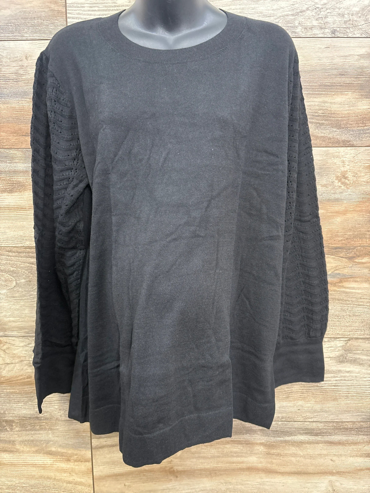 Black long sleeve sweater with textured openwork sleeves on mannequin against wood wall